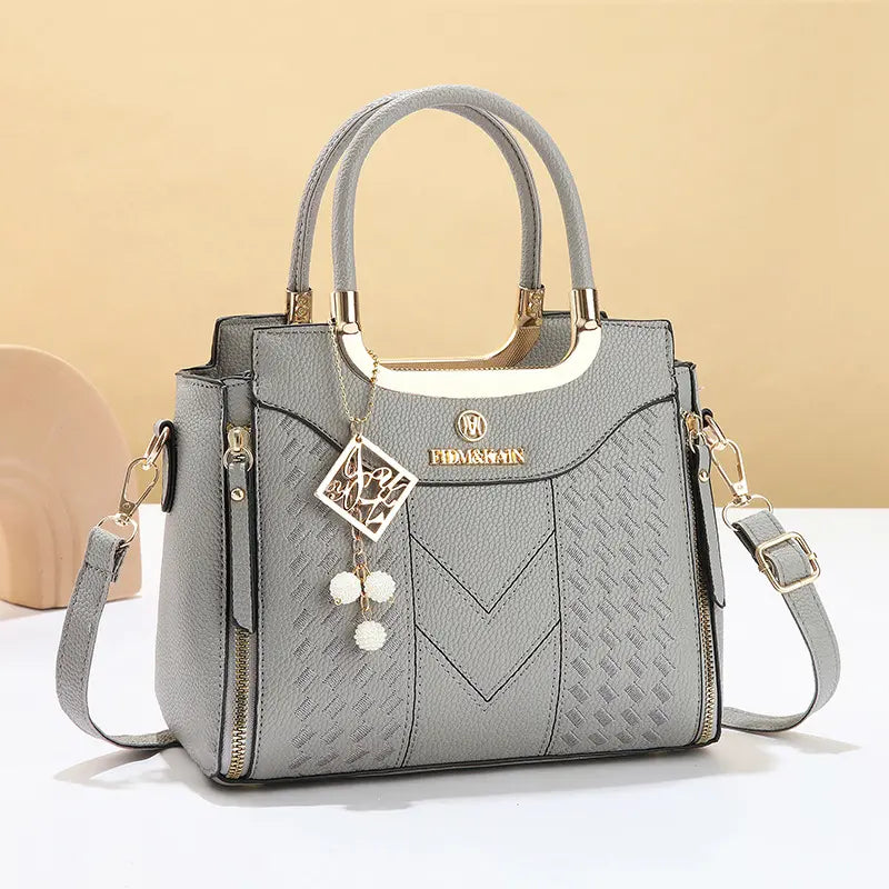 Dámska crossbody kabelka s prešívaním v tvare písmena V, kovaniami v zlatej farbe, viacerými priehradkami a hornou rukoväťou.