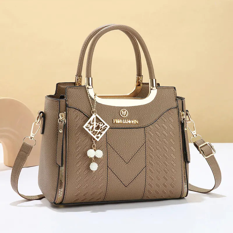 Dámska crossbody kabelka s prešívaním v tvare písmena V, kovaniami v zlatej farbe, viacerými priehradkami a hornou rukoväťou.