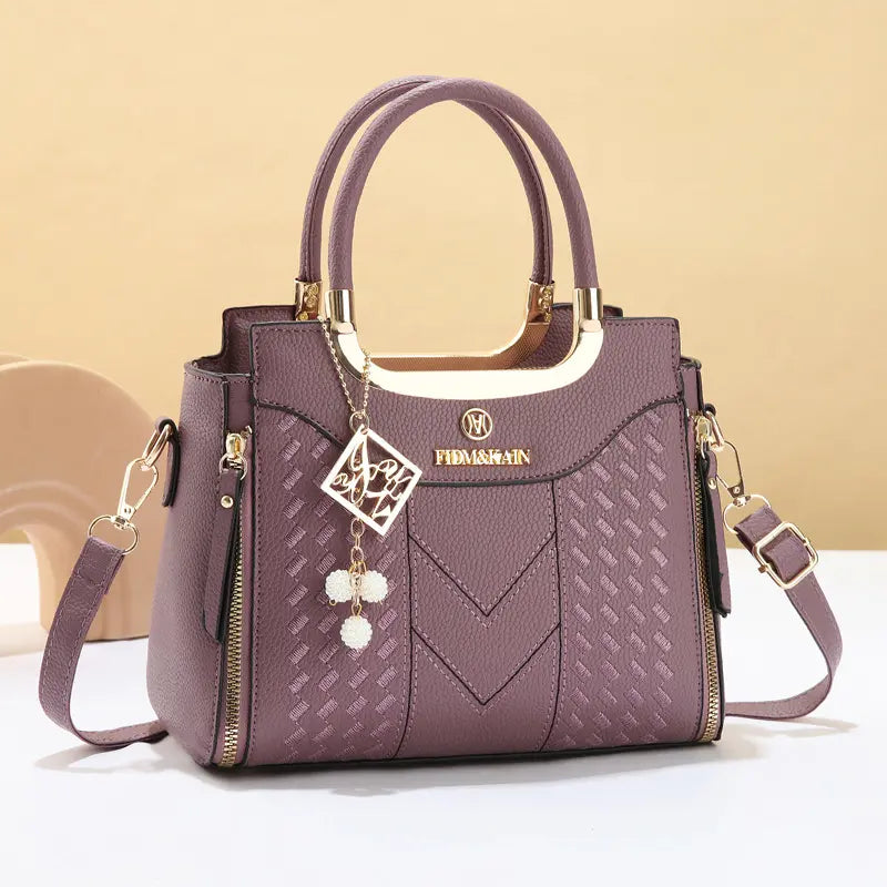 Dámska crossbody kabelka s prešívaním v tvare písmena V, kovaniami v zlatej farbe, viacerými priehradkami a hornou rukoväťou.